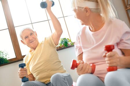 Senior couple exercise together at home doing aerobics lift up dubbells smilingの写真素材