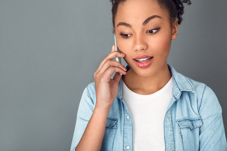 Young african woman isolated on grey wall studio casual daily lifestyle phone communicationの写真素材