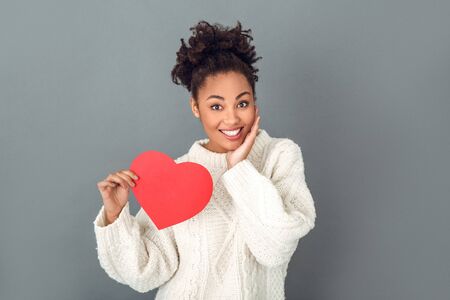 Young african woman isolated on grey wall studio winter concept holding hear flirtingの写真素材