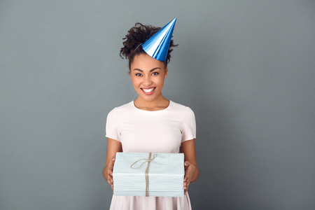 Young african woman isolated on grey wall studio celebration concept holding present boxの写真素材