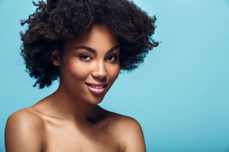 Young african woman isolated on blue wall studio fashion photoshoot smilingの写真素材