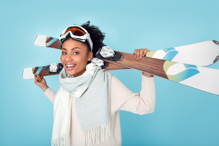 Young african woman isolated on blue wall studio winter sport skiing standing with skis side viewの写真素材