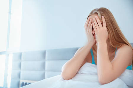 Young woman at home sitting on bed woke up sleepyの写真素材