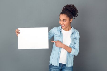 Young african woman isolated on grey wall studio casual daily lifestyle showing paperの写真素材