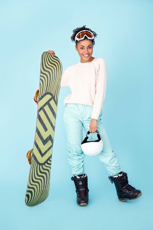 Young african woman isolated on blue wall studio winter sport snowboarding concept fully equipedの写真素材