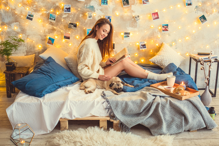 Young woman weekend at home decorated bedroom stroking dog reading bookの写真素材