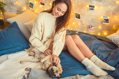 Young woman weekend at home decorated bedroom playing with dogの写真素材