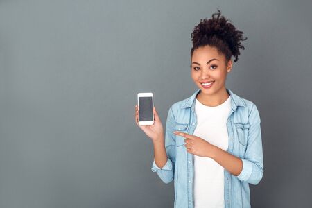 Young african woman isolated on grey wall studio casual daily lifestyle holding smartphoneの写真素材