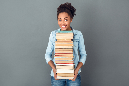 Young african woman isolated on grey wall studio casual daily lifestyle holding books exam preparationの写真素材