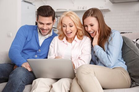 Young family with mother-in-law at home weekend browsing laptop smiling