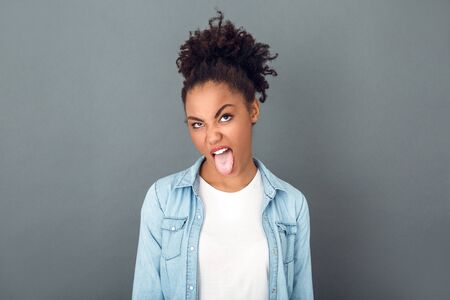 Young african woman isolated on grey wall studio casual daily lifestyle unsatisfied tongue outの写真素材