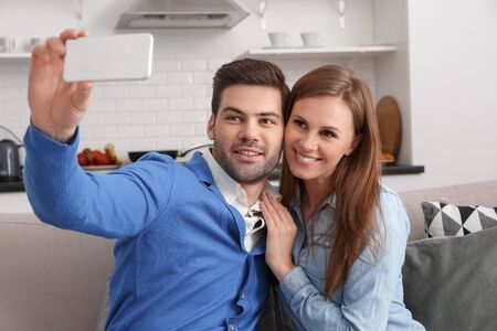 Young couple together at home weekend holding smartphone taking selfiesの写真素材