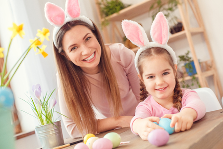 Mother and daughter in bunny ears easter celebration together at home sitting looking camera smilingの写真素材