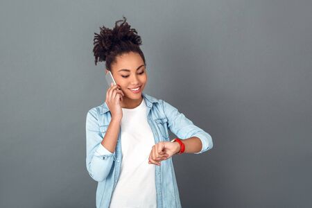 Young african woman isolated on grey wall studio casual daily lifestyle looking at watchの写真素材