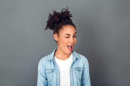Young african woman isolated on grey wall studio casual daily lifestyle winkingの写真素材