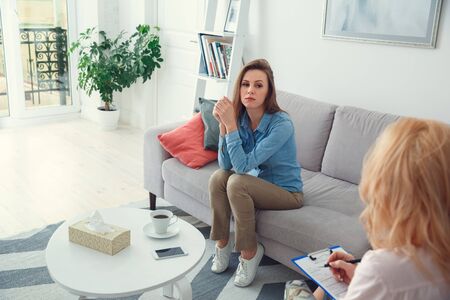Female psychologyst therapy session with client indoors sitting taking notesの写真素材