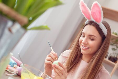Young woman at home easter celbration concept in a bunny ears sitting coloring eggs painting dotsの写真素材