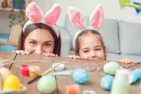 Mother and daughter together in bunny ears at home easter celebration hiding under tableの写真素材