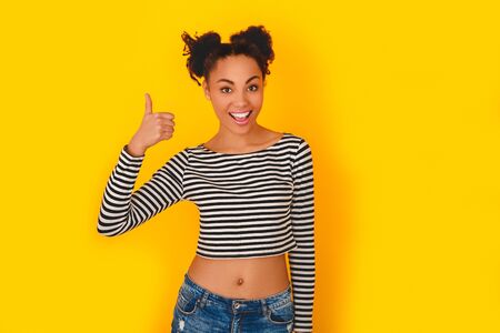 Young african woman isolated on yellow wall studio teen style thumb upの写真素材