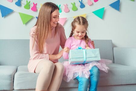 Mother and daughter together celebration at home sitting on sofa girl holding present box from momの写真素材