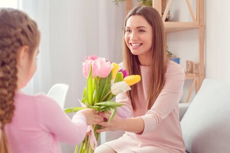 Mother and daughter together at home moms birthday girl giving a bunch of tulipsの写真素材