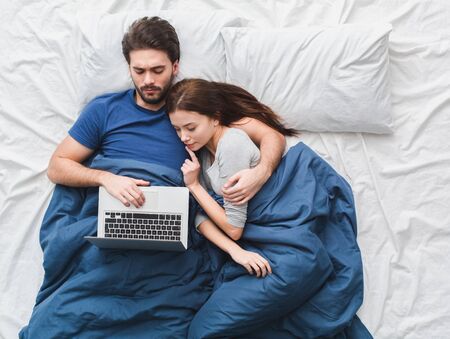 Young couple in bed top view morning concept watching movie on laptopの写真素材