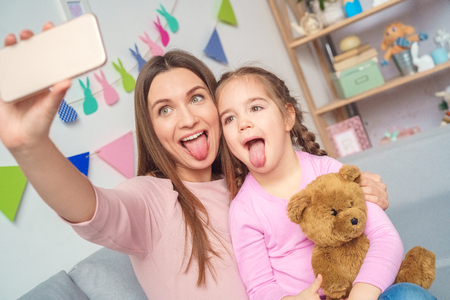 Mother and daughter together at home taking pictures on smartphoneの写真素材