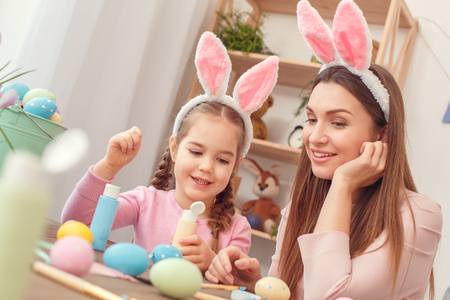 Mother and daughter together easter preparation at home sitting in bunny ears discussing designの写真素材