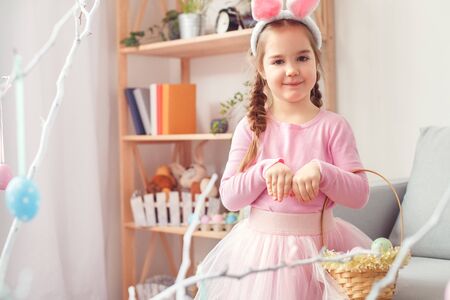 Little cute girl in bunny ears and dress at home easter celebration concept holding basket with eggsの写真素材