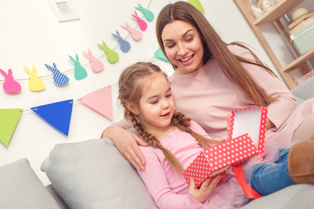Mother and daughter together at home celebration concept sitting girl looking inside gift box surprisedの写真素材
