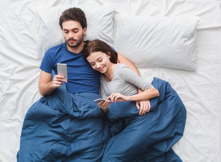 Young couple in bed top view morning concept browsing smartphonesの写真素材