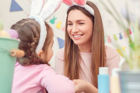 Mother and daughter together at home easter preparation in bunny ears looking at each other happyの写真素材