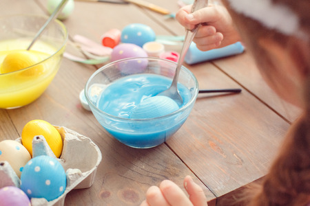 Little cute girl at home easter celebration concept back view close-up coloring eggs dipping egg...