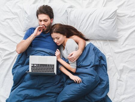 Young couple in bed top view morning concept watching videos on laptopの写真素材