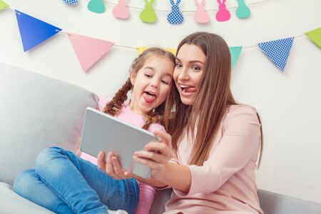Mother and daughter together weekend at home sitting holding digital tablet taking selfie picturesの写真素材