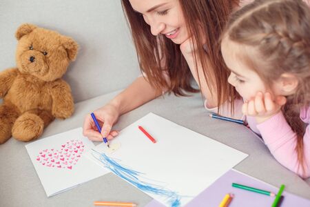 Mother and daughter weekend together at home on sofa mom help to draw greeting cardの写真素材