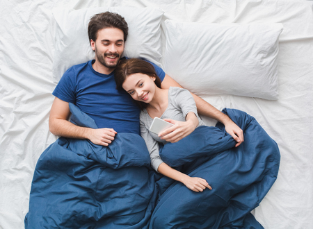 Young couple in bed top view morning concept girl taking selfie photosの写真素材