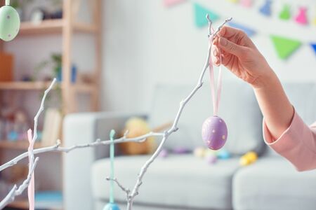 Young woman at home easter celebration concept hanging egg on treeの写真素材