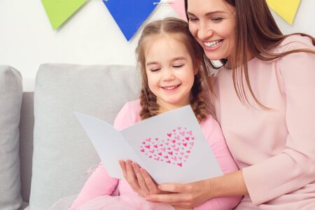 Mother and daughter together at home celebration concept sitting reading greeting cardの写真素材