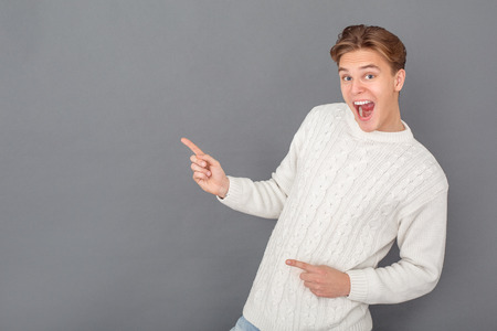 Young man wearing sweater studio isolated on grey pointing at free spaceの写真素材