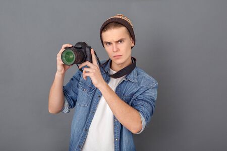 Young male photographer in jeans jacket studio isolated on grey holding camera upの写真素材