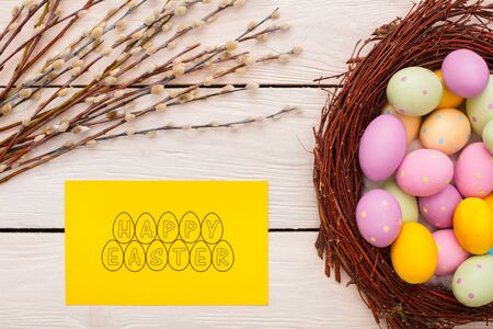 Easter traditional objects isolated on wooden floor colorful eggs in nest willow branches in the corner and creative greeting card happy easter top viewの写真素材