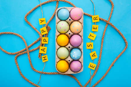Easter objects colorful eggs in a box isolated on blue background surrounded by rope and paper letters happy easterの写真素材
