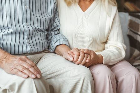 Senior couple together at home sitting holding hands close-upの写真素材