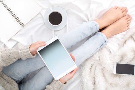 Young woman sitting on bed top view holding digital tablet playing online games