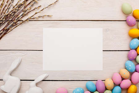 Easter traditional objects isolated on wooden floor white paper surrounded by colorful eggs willow branches and rabbi figurinesの写真素材