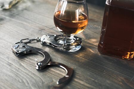Alcohol addiction objects isolated on table no people glass of whiskey fasten by handcuffs close-upの写真素材
