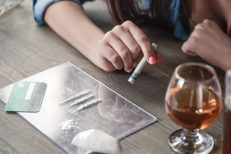 Young female drug addicted social problems sitting at table doses prepared before use and glass of...