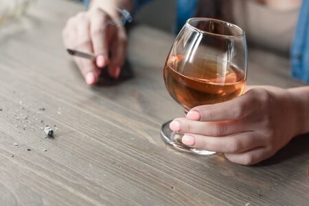 Young female alcoholic smoker social problems sitting at table smoking and drinking whiskey ash close-upの写真素材