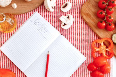 Many vegetables on the table and a notebook with an inscription cooking. Indoor, studio shoot, kitchen interiorの写真素材